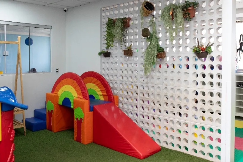 Espaço de recreação com escorregador em formato de arco-íris e plantas
