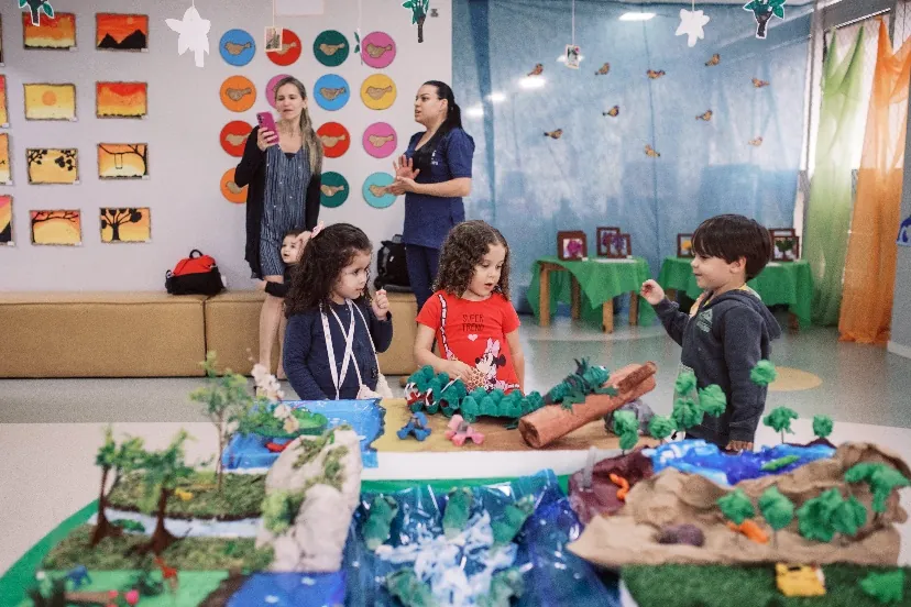 Crianças em atividade pedagógica com maquete, acompanhadas por professoras